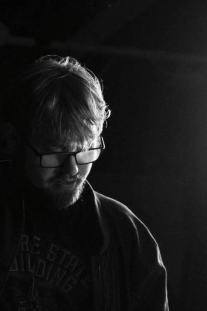 Patrick Turnbull in a black and white photo looking down while a bright white light illuminates one side of his face.